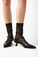 Black high-heeled shoes worn with sheer black socks on a white background
