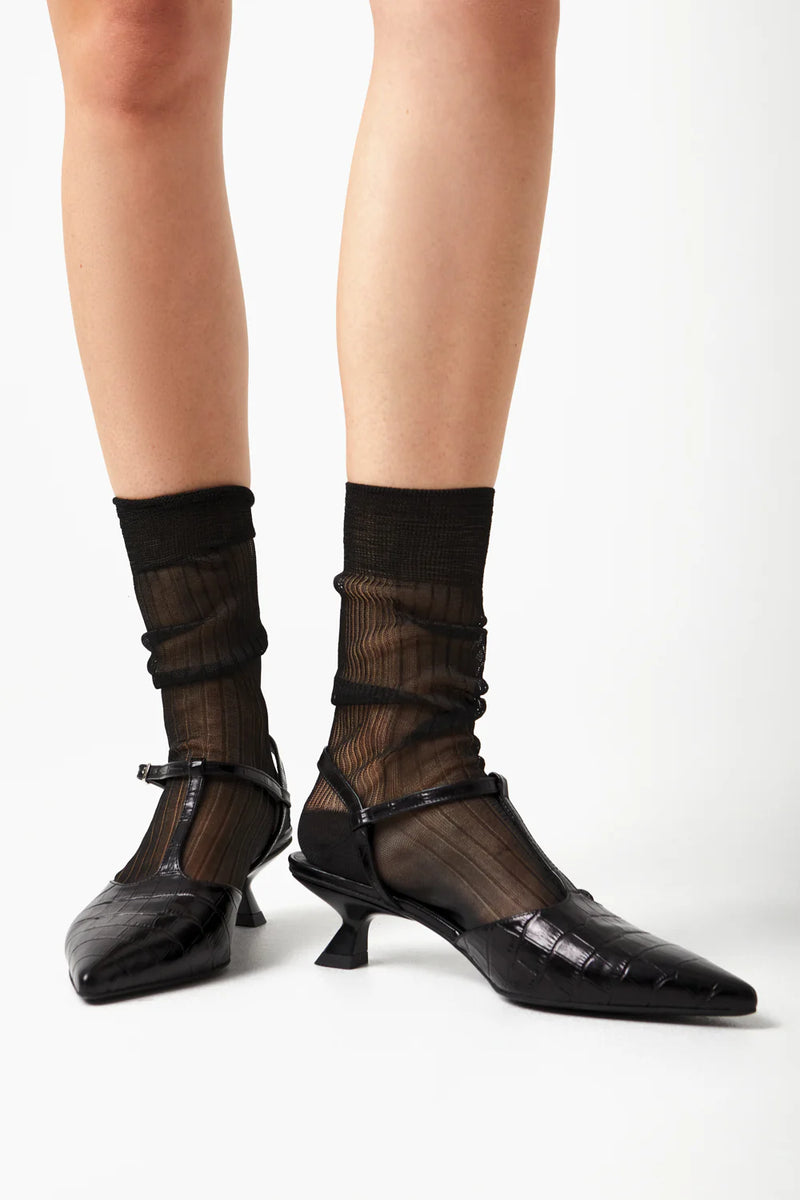 Black high-heeled shoes worn with sheer black socks on a white background