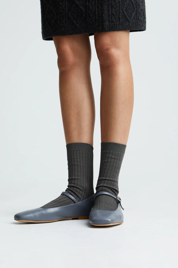Person wearing gray socks and flat shoes on a white background