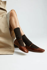 Person wearing black socks and brown shoes with a neutral background
