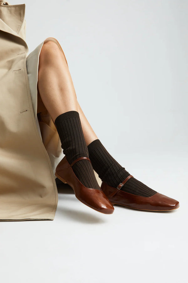 Person wearing black socks and brown shoes with a neutral background