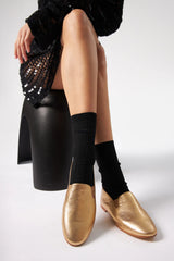 Person wearing gold loafers and black socks with a black sequin clutch on a white background