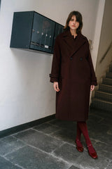 Woman in a long dark coat standing in a stairwell.