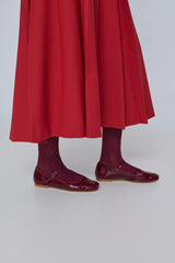 Person wearing a red skirt and maroon shoes on a white background