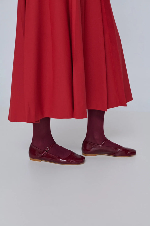 Person wearing a red skirt and maroon shoes on a white background