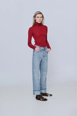 Person wearing a red turtleneck sweater and light blue jeans on a white background