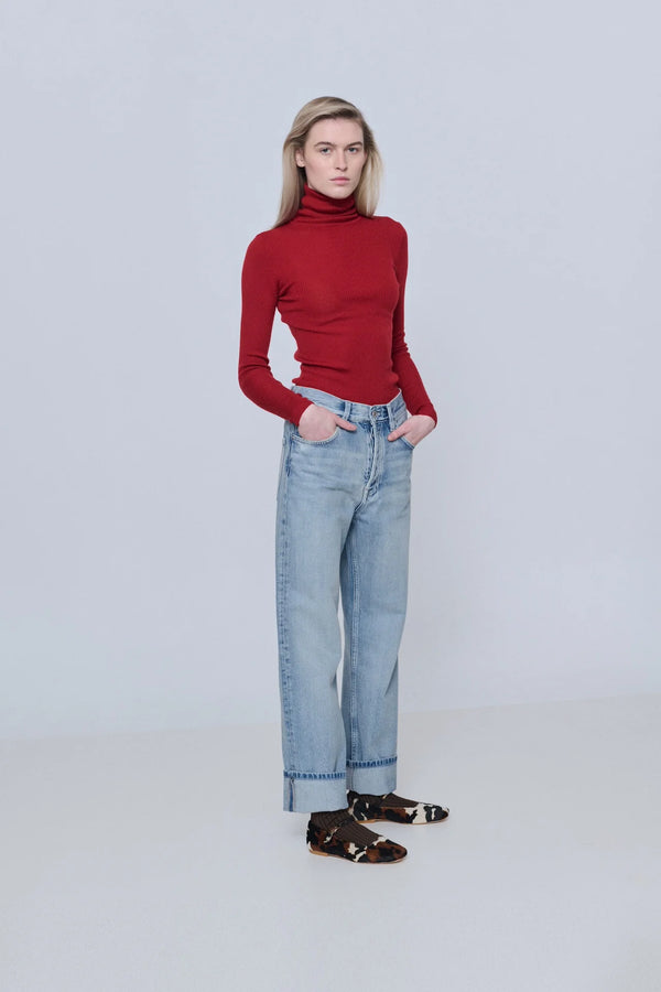 Person wearing a red turtleneck sweater and light blue jeans on a white background
