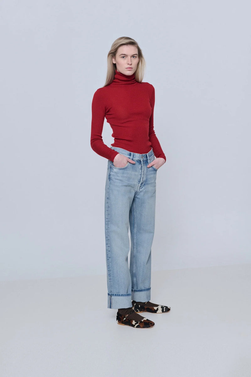 Person wearing a red turtleneck sweater and light blue jeans on a white background