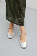 Silver shoes worn with a green sequin skirt on a gray background