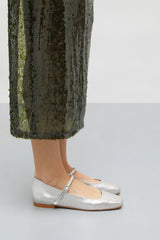 Silver flats worn with green sequin pants on a plain background