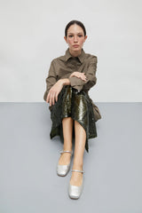 Woman sitting on a gray surface wearing a brown shirt and green sequin skirt.