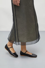 Person wearing a long dark green dress and black shoes on a light gray background