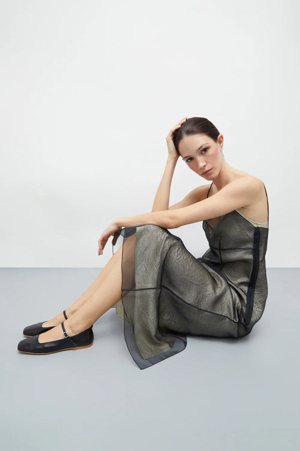 Woman sitting on a gray floor wearing a black dress with sheer panels.