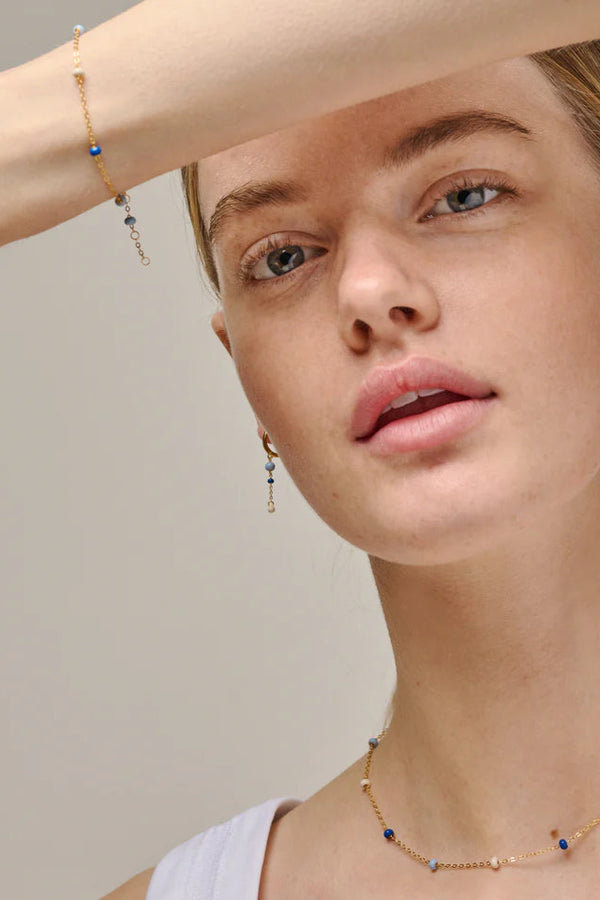 Close-up of a woman wearing gold jewelry with small beads on a neutral background
