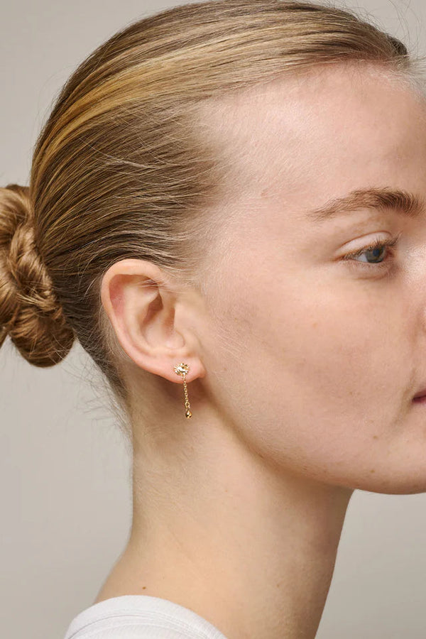 Close-up of a person wearing gold earrings with a neutral background