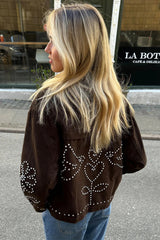 Person wearing a brown jacket with decorative elements, standing on a street.