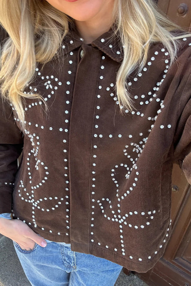 Brown suede jacket with white stitching worn by a person, standing against a wooden door.