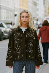 Woman wearing a dark brown jacket with white patterns on a city street.