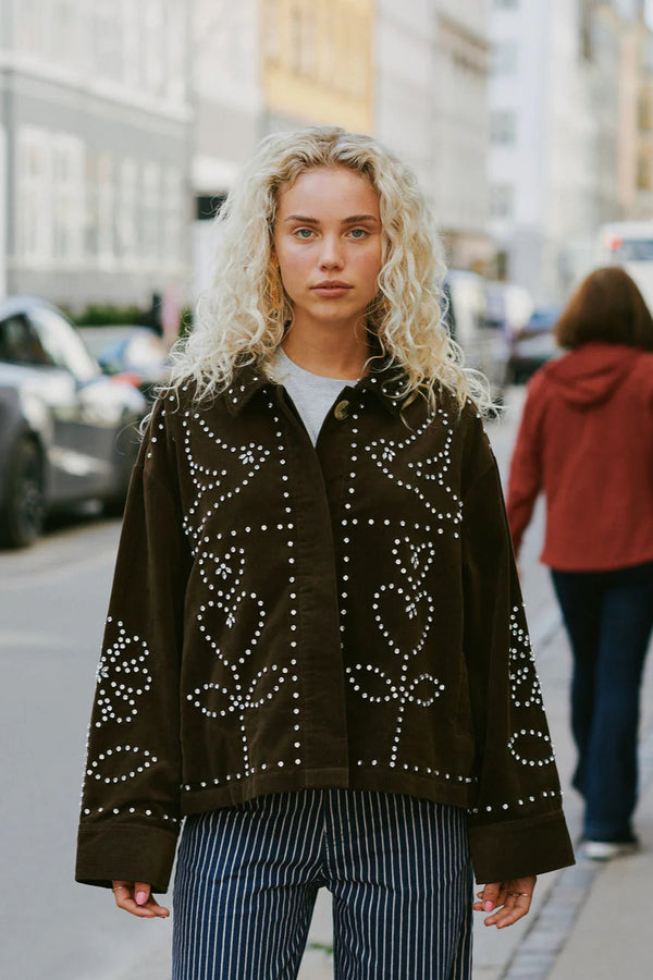 Woman wearing a dark brown jacket with white patterns on a city street.