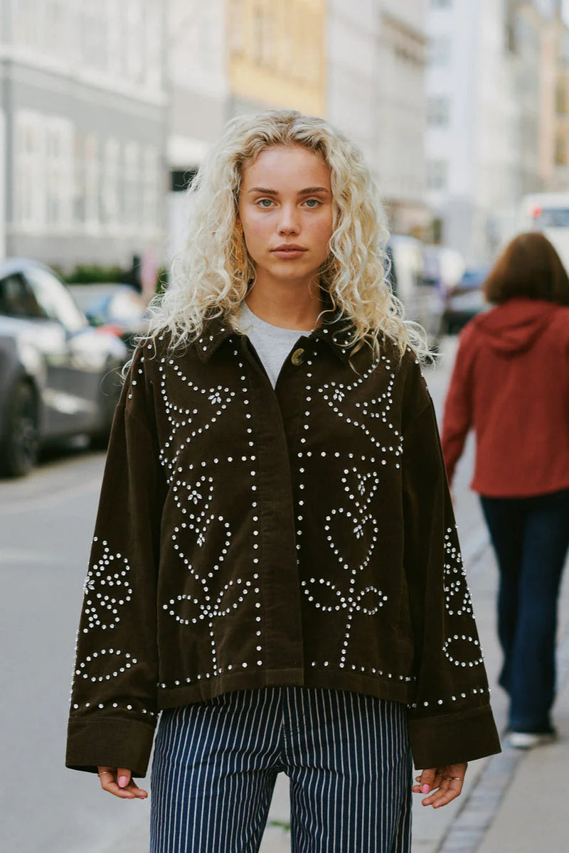 Woman wearing a dark brown jacket with white patterns on a city street.