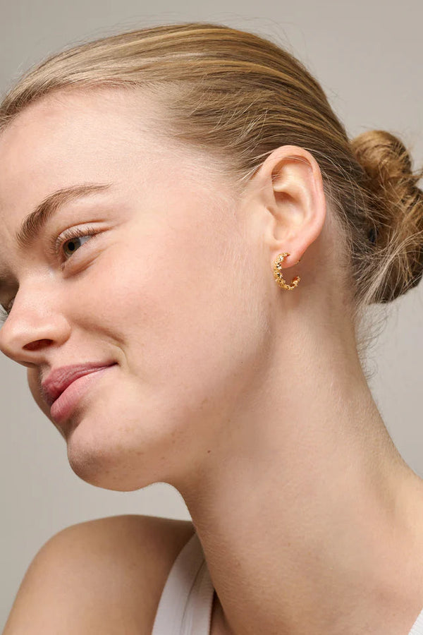 Close-up of a woman wearing gold hoop earrings against a neutral background