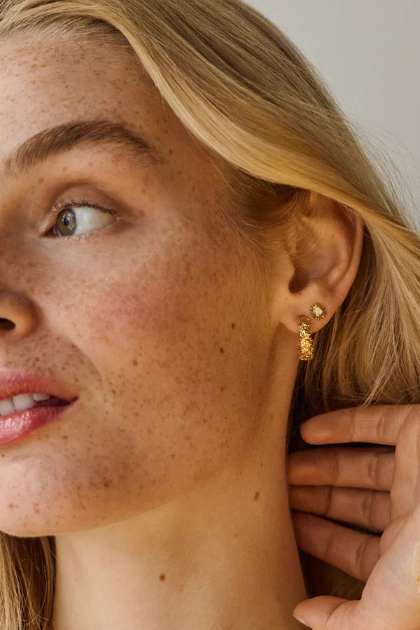 Close-up of a woman wearing gold earrings with a neutral background