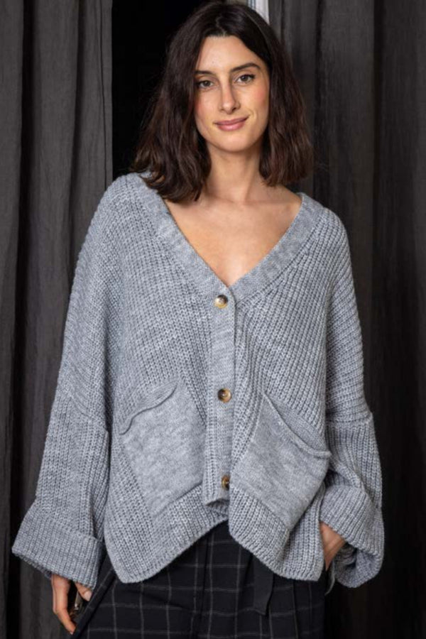 Woman wearing a gray knitted cardigan against a dark background
