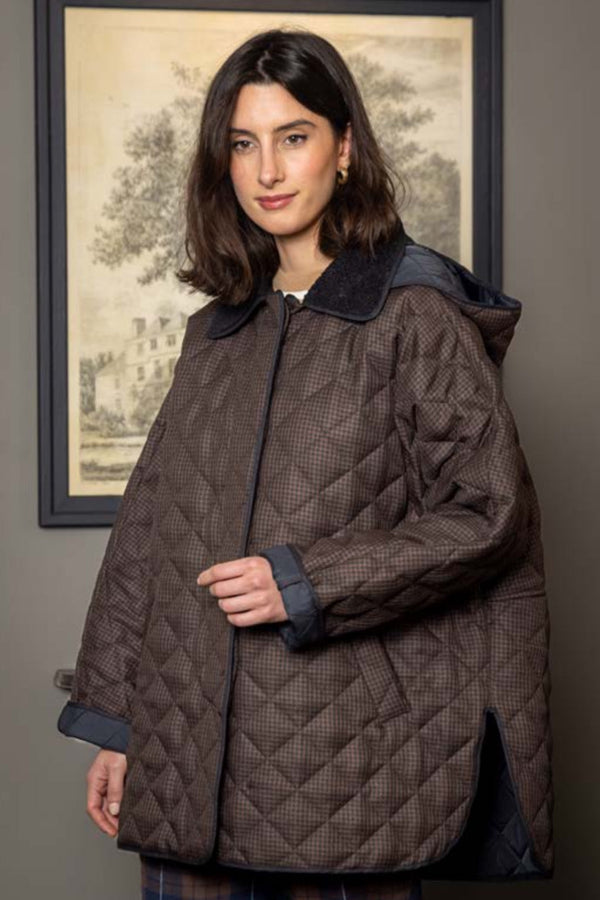 Woman wearing a quilted coat standing in front of a framed picture on a wall.