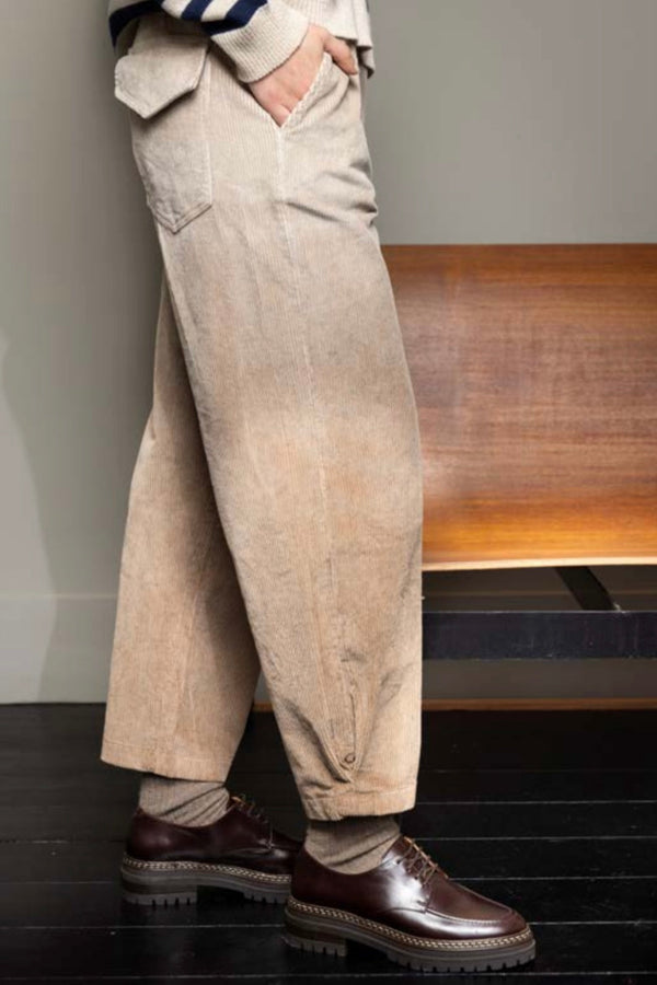 Person wearing beige wide-leg pants and brown shoes in a minimal indoor setting.