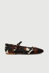 Cow print flat shoe with a strap on a light gray background