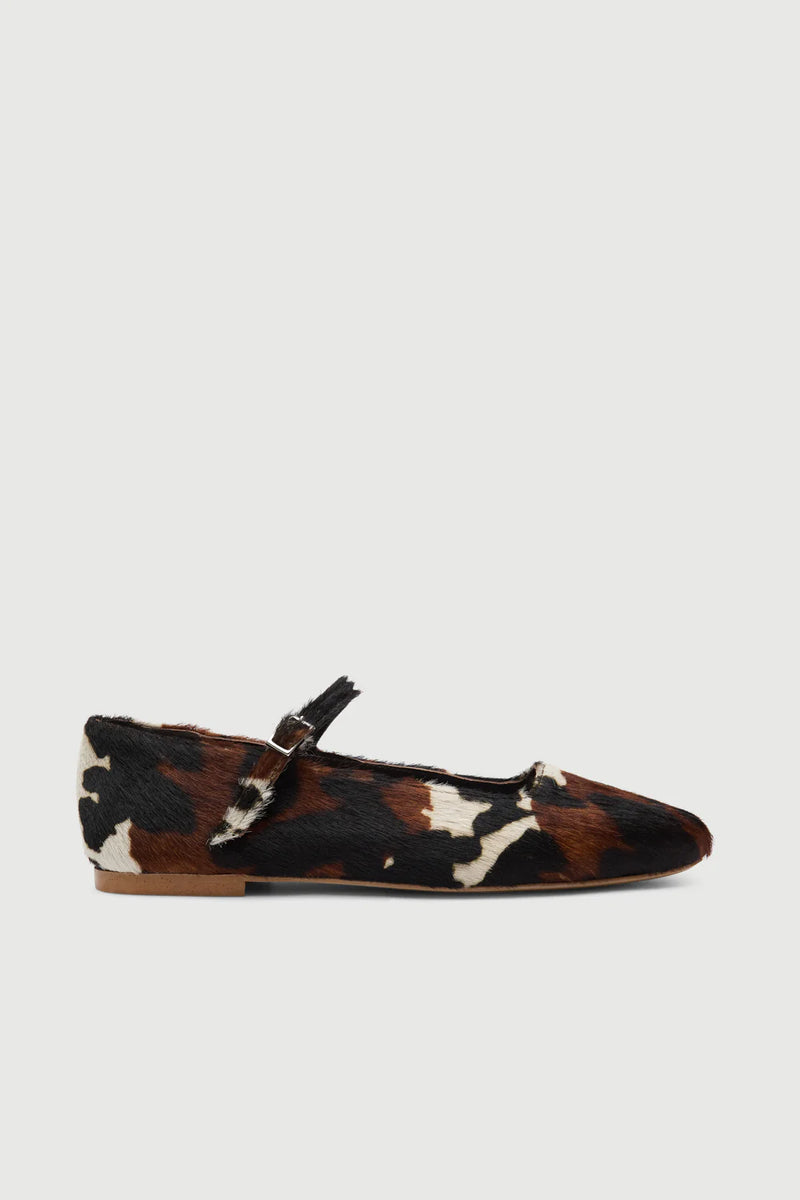 Cow print flat shoe with a strap on a light gray background