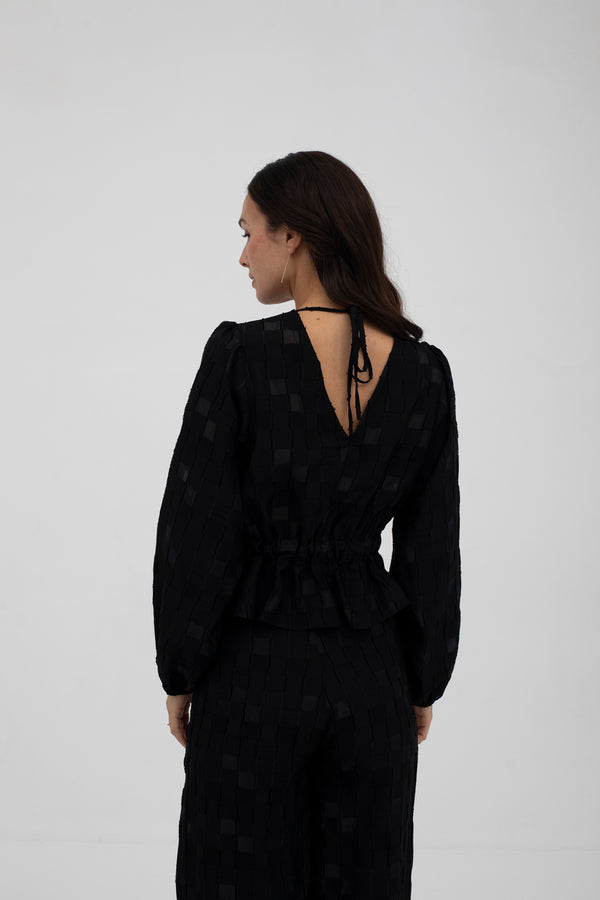 Woman wearing a black outfit with long sleeves and a V-neckline on a plain background