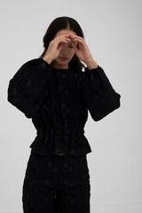 Person wearing a black textured outfit on a plain background
