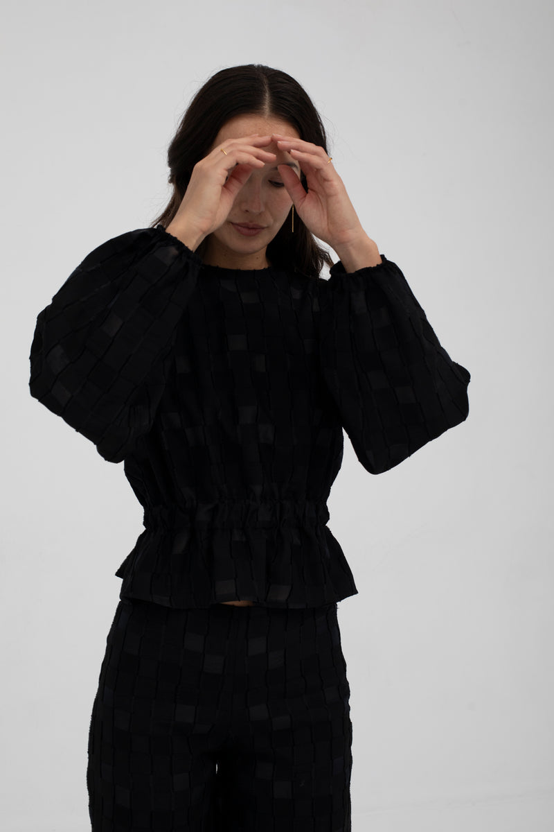 Person wearing a black textured outfit on a plain background