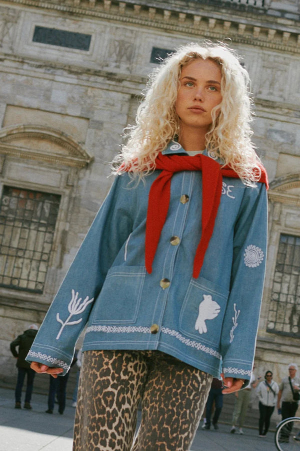 Person wearing a blue jacket with white patterns and a red scarf in front of a building.