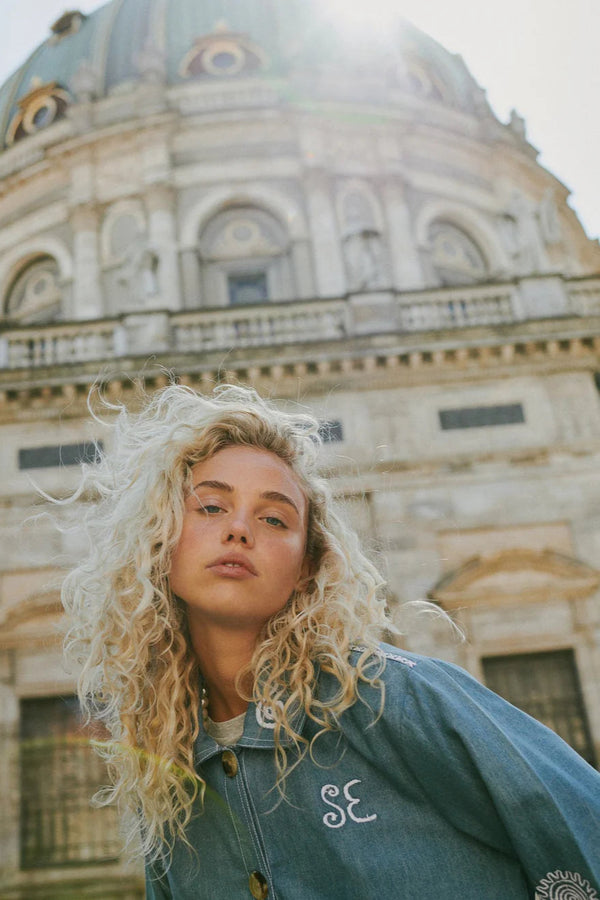Woman with curly blonde hair in front of a large architectural building