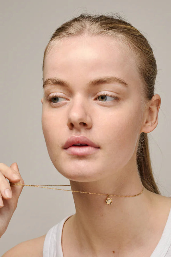 Woman wearing a delicate gold necklace against a neutral background