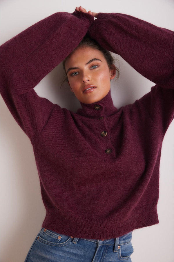 Woman wearing a burgundy sweater with button details against a plain background