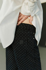 Person wearing a white blazer and black polka dot pants with a blurred background