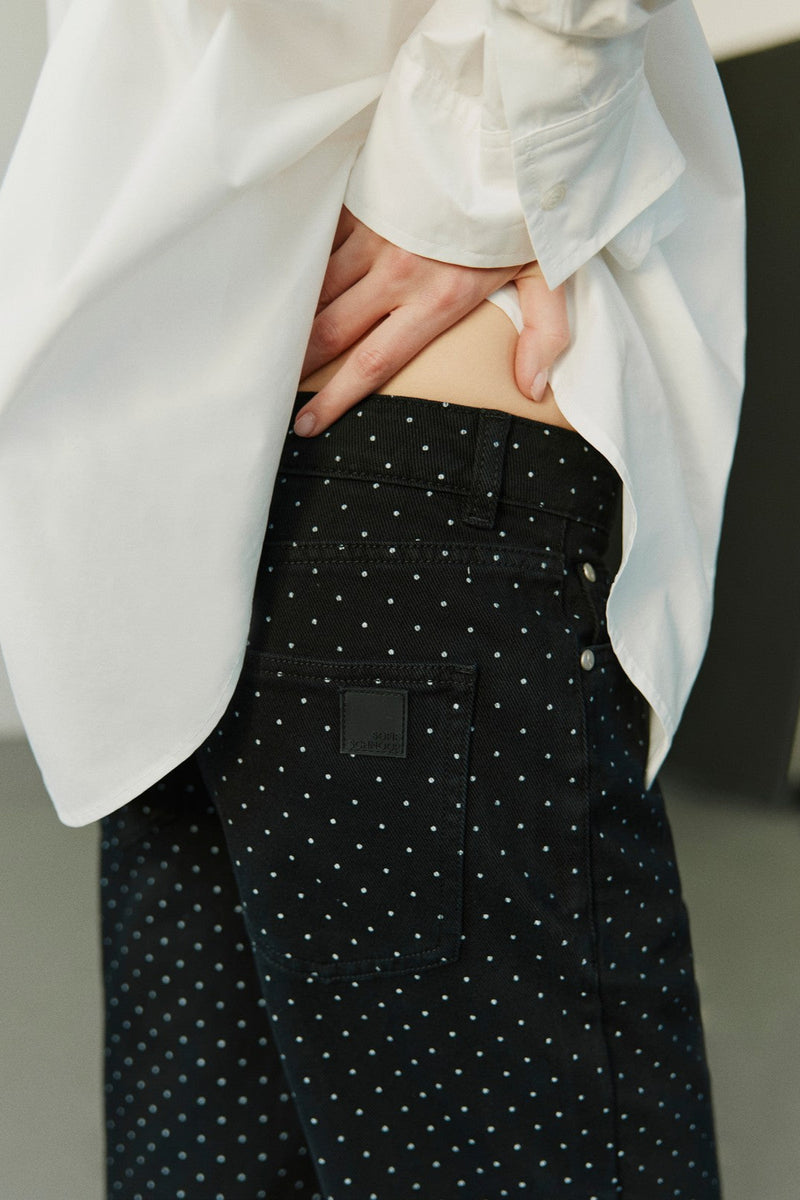 Person wearing a white blazer and black polka dot pants with a blurred background