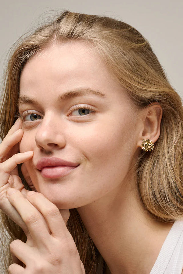 Close-up of a woman with blonde hair and a gold earring, touching her face.