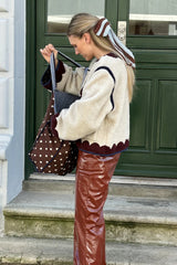 Woman in a cream jacket and brown pants holding a polka dot bag on a staircase.