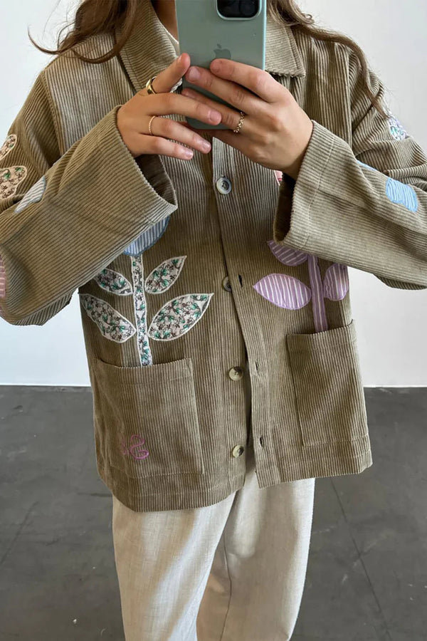 Person wearing a brown corduroy jacket with colorful patch designs, taking a mirror selfie.