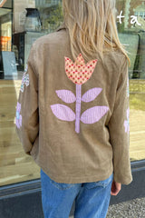 Person wearing a brown jacket with a floral design on the back, standing in front of a store window.