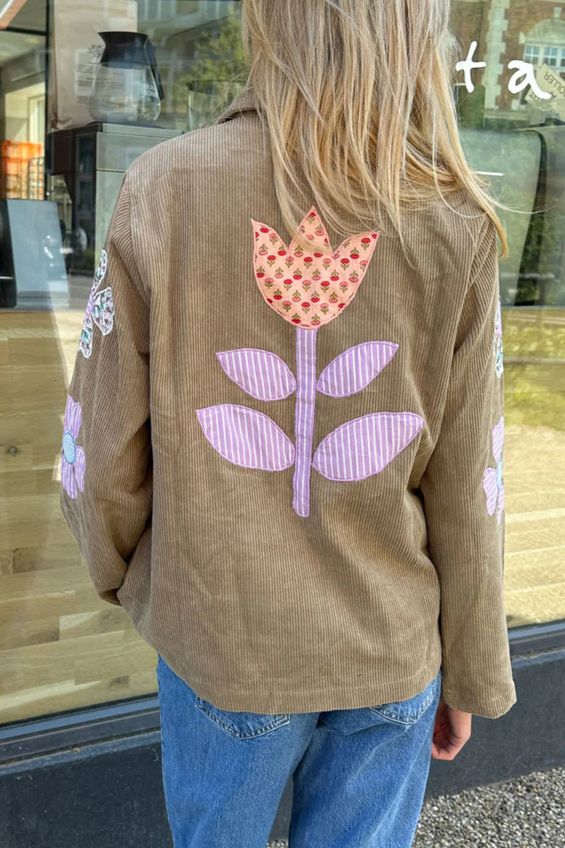Person wearing a brown jacket with a floral design on the back, standing in front of a store window.