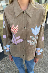 Person wearing a brown corduroy jacket with floral appliqués in an outdoor setting