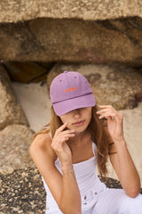 Woman wearing a purple cap with text, sitting on stone steps.