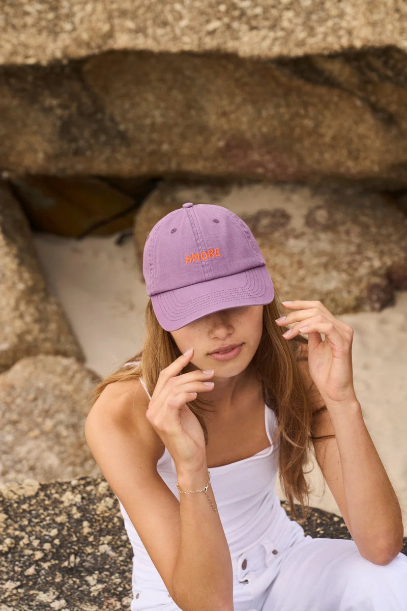 Woman wearing a purple cap with text, sitting on stone steps.