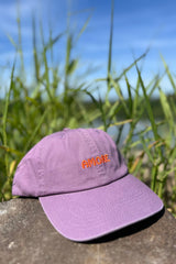 Purple cap with 'AMORE' text on a stone surface with grass and blue sky in the background