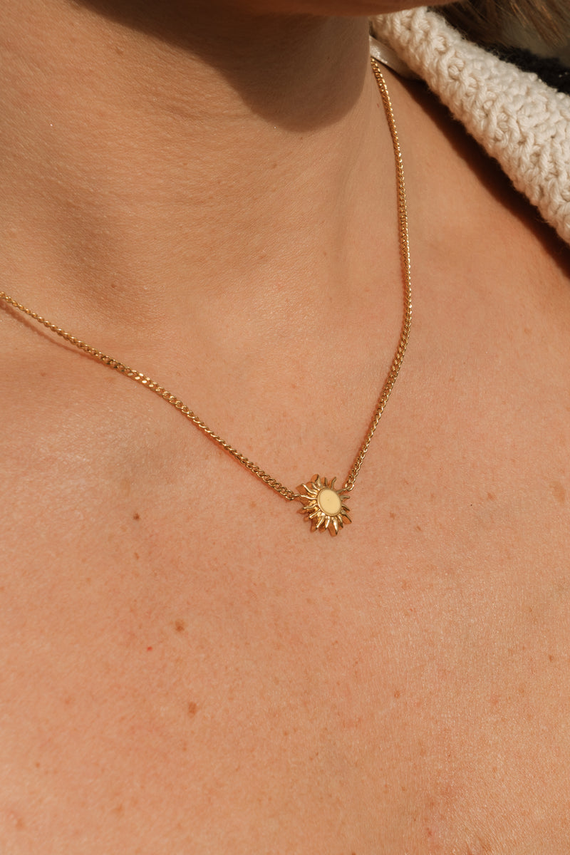 Gold necklace with a sun pendant on a person's neck